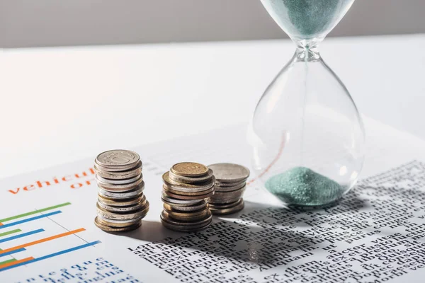 Стопки монет и песочные часы на бизнес-документе с серым фоном — стоковое фото