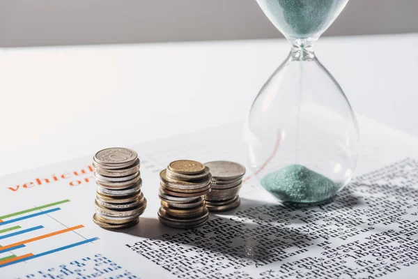 Coins stacks and hourglass on business document with grey background — Stock Photo