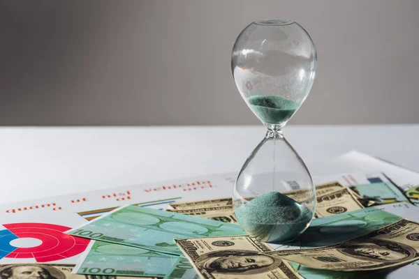 Hourglass and coins staks on dollar and euro banknotes with grey background — Stock Photo