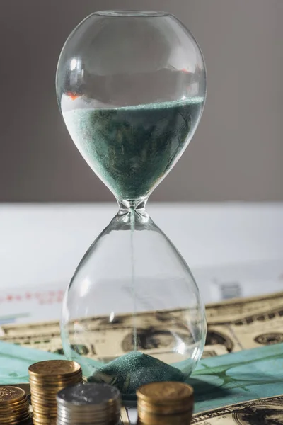 Пісочний годинник і монети стоять на банкнотах з розмитим фоном — стокове фото