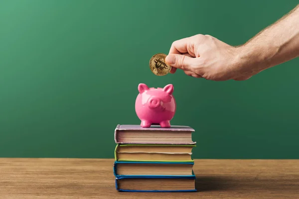 Uomo puting moneta in salvadanaio rosa su libri con sfondo verde — Foto stock
