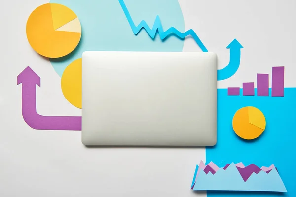 Top view of closed laptop and charts and graphs, pointers made of paper on white background — Stock Photo