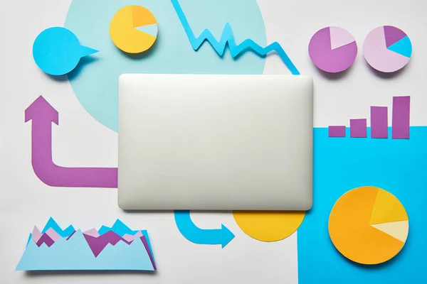 Top view of laptop, charts and graphs, pointers made of paper on white background — Stock Photo