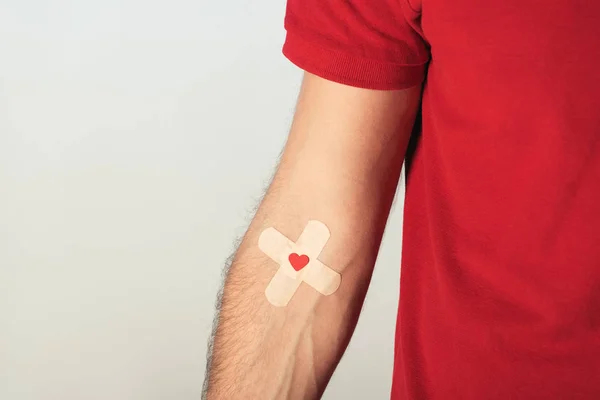 Partial view of patient in red t-shirt with plasters on grey background, blood donation concept — Stock Photo