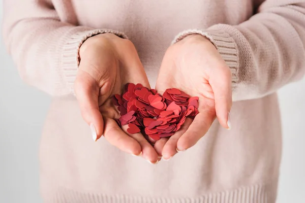 Partial view of woman in pink sweater holding paper hearts on grey background — Stock Photo