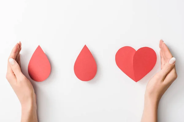 Vista parcial de la mujer sosteniendo el corazón de papel y gotas sobre fondo blanco - foto de stock