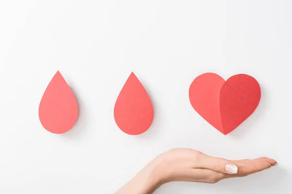 Vista recortada de la mujer sosteniendo el corazón de papel y gotas sobre fondo blanco - foto de stock