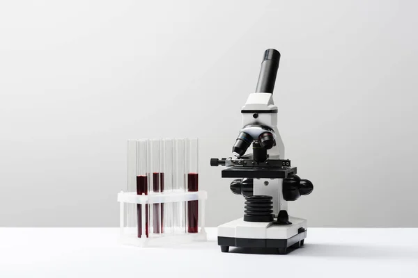 Microscópio e tubos de ensaio com sangue sobre fundo cinzento — Fotografia de Stock