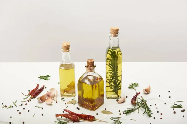 Varie bottiglie di olio aromatizzato con diverse spezie e rosmarino su superficie bianca — Foto stock