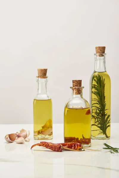 Different bottles with oil flavored with various spices and rosemary on white surface — Stock Photo