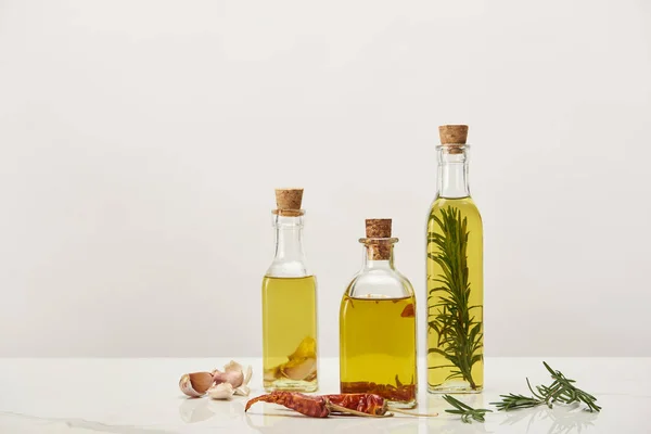 Botellas de aceite aromatizado con romero y varias especias en la superficie blanca - foto de stock