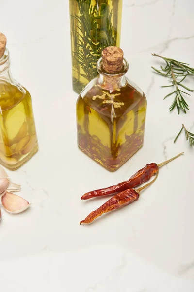 Botellas de aceite de corcho aromatizado con romero y diferentes especias en la superficie blanca - foto de stock