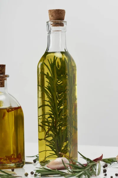 Diferentes garrafas de forma de óleo aromatizado com alecrim e especiarias diferentes no fundo cinza — Fotografia de Stock