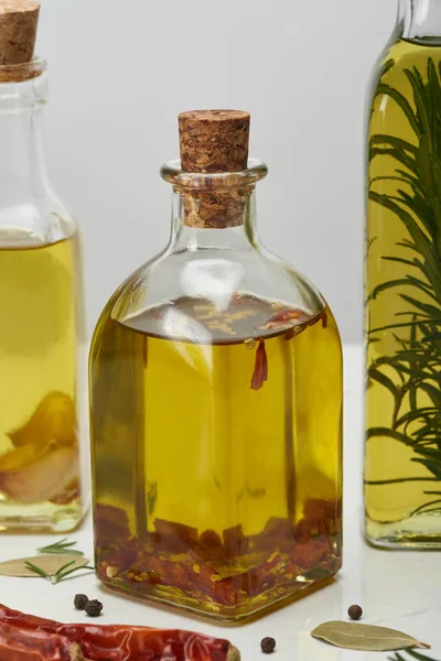 Varias botellas de aceite aromatizado con diferentes especias y romero en la superficie blanca - foto de stock