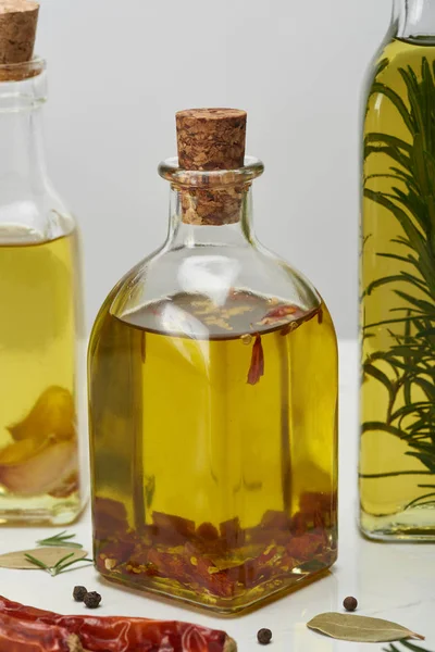 Various bottles of oil flavored with different spices and rosemary on white surface — Stock Photo