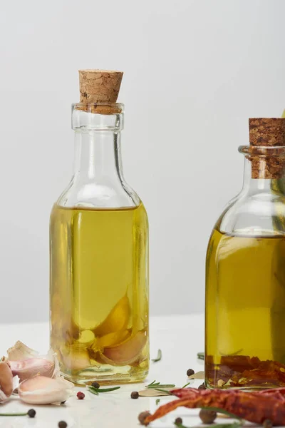 Diverses bouteilles d'huile aromatisées avec différentes épices et romarin sur surface blanche — Photo de stock