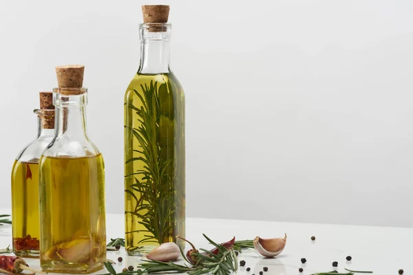 Different bottles of oil flavored with various spices and rosemary on white surface — Stock Photo