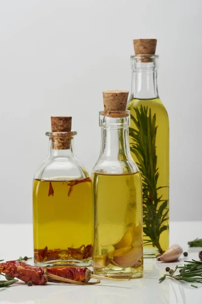 Bottles of oil flavored with rosemary and various spices on white surface — Stock Photo