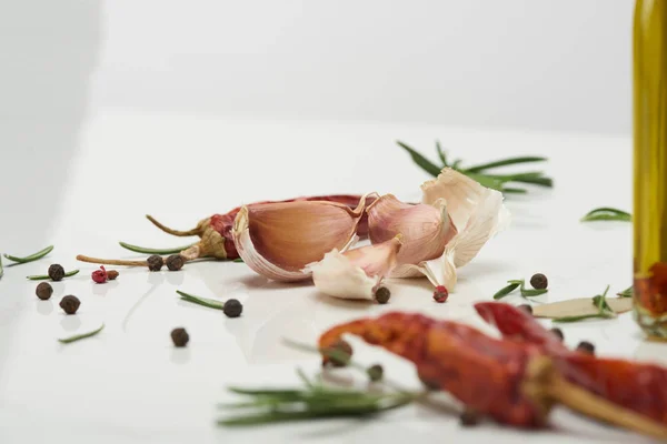 Knoblauchzehen, Rosmarinblätter, Chilischote und schwarzer Pfeffer auf weißer Oberfläche — Stockfoto