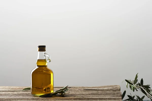 Flasche Öl und Olivenbaumblätter isoliert auf grau — Stockfoto