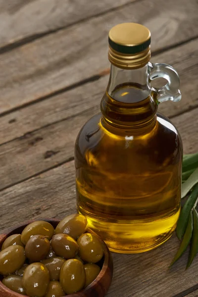 Botella de aceite, tazón de aceitunas y hojas de olivo en la superficie de madera - foto de stock