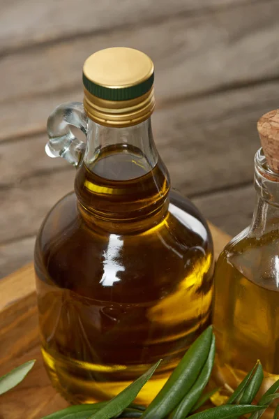 Bandeja de madera con botellas de aceite de oliva y hojas de olivo en la superficie de madera - foto de stock