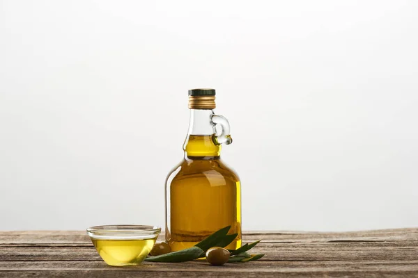 Garrafa e tigela com óleo, azeitonas e folhas de oliveira isoladas em cinza — Fotografia de Stock