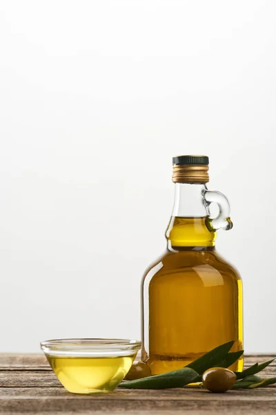 Tazón y botella de aceite, hojas de olivo y aceitunas aisladas en gris - foto de stock