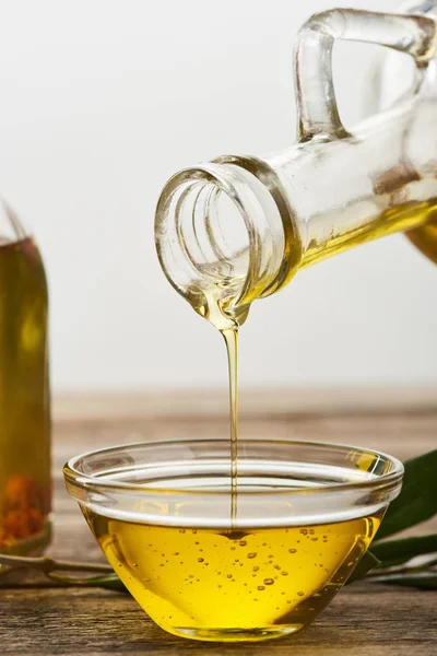 Pouring olive oil from bottle into glass bowl on wooden surface — Stock Photo