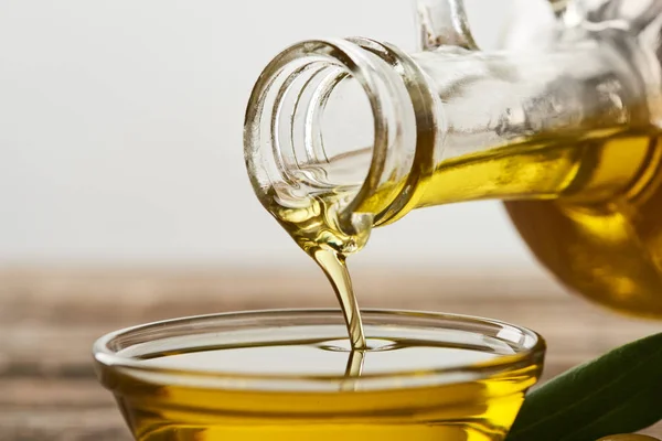 Verter el aceite de oliva de la botella en un recipiente de vidrio sobre un fondo gris - foto de stock