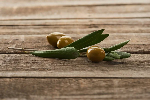 Olive tree branch and green olives on wooden surface — Stock Photo