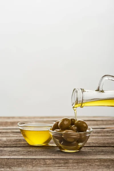 Verser dans un bol en verre avec des olives, et un bol plein d'huile sur la surface en bois — Photo de stock