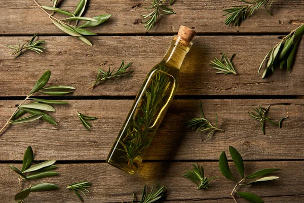 Vista superior de la botella con aceite aromatizado y ramas de romero sobre fondo de madera - foto de stock