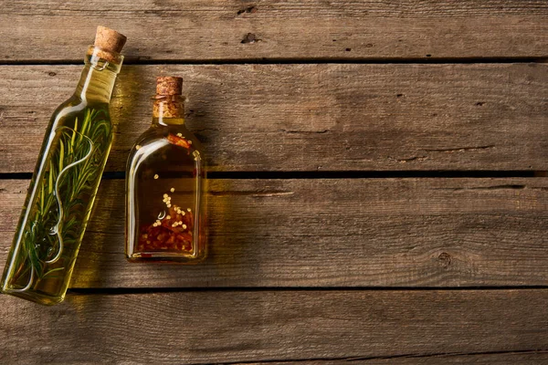 Top view of bottles with oil flavored with rosemary and spices on wooden background — Stock Photo