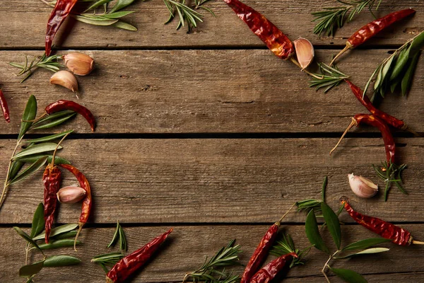 Top view of red hot chili peppers, rosemary branches and garlic cloves on wooden background — Stock Photo