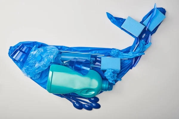 Vista superior de la figura de ballena hecha de guantes de goma, vajilla de plástico desechable, bolsa, esponjas y botella aislada en blanco - foto de stock