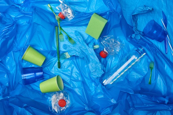 Vista superior de la bolsa de polietileno arrugado azul con botellas de plástico, vajilla desechable y esponja - foto de stock