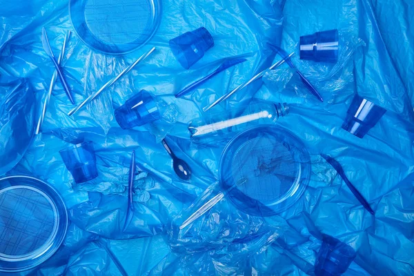Vista dall'alto del sacchetto di polietilene blu stropicciato con bottiglie di plastica, tazze, piatti, coltelli, cucchiaio ang spugna — Foto stock