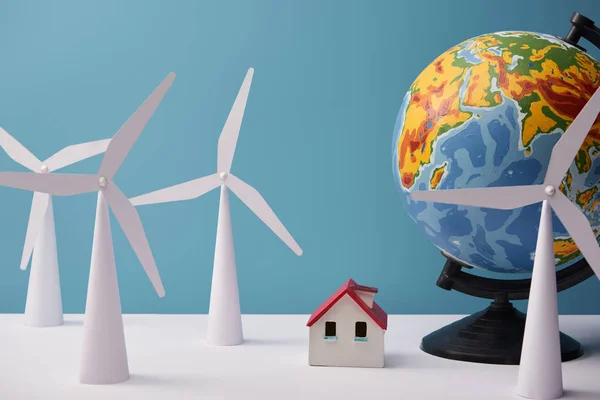 Windmill and house models with globe on white table and blue background — Stock Photo
