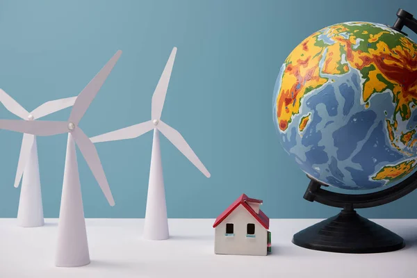 Windmill and house models with big globe on white table and blue background — Stock Photo