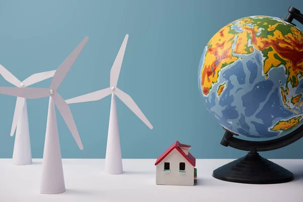 Moulin à vent et modèles de maison avec grand globe sur table blanche et fond bleu — Photo de stock