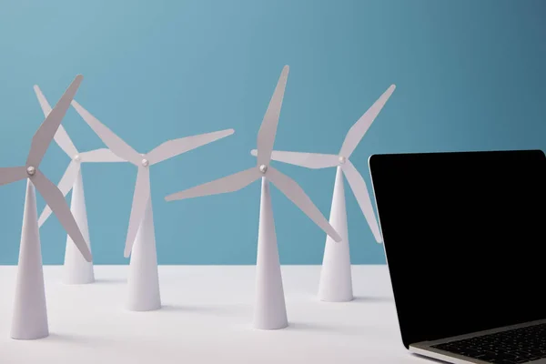 Portátil sobre mesa blanca con modelos de molino de viento sobre fondo azul — Stock Photo