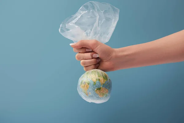 Cropped view of woman holding globe in plastic clear bag on blue background — Stock Photo