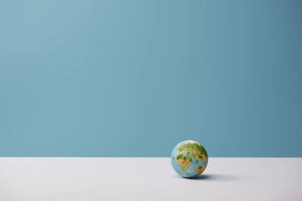 Small globe on white table and blue background — Stock Photo