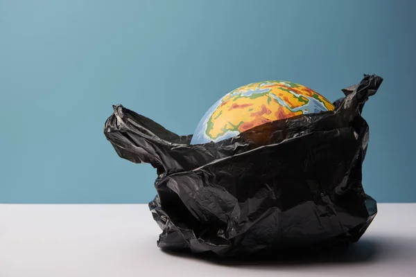 Globus in schwarzer Polyethylen-Tasche auf weißem Tisch und blauem Hintergrund — Stockfoto