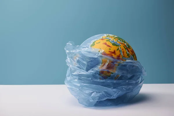 Земной шар в полиэтиленовой сумке на белом столе и синем фоне — стоковое фото