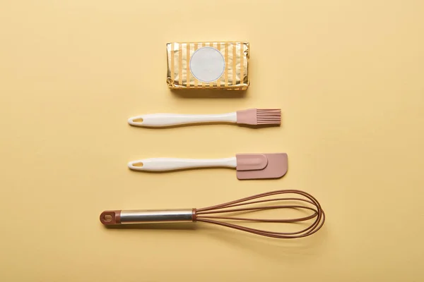 Flat lay with butter, balloon whisk, spatula and bakery brush on yellow background — Stock Photo