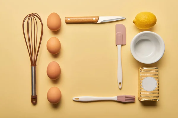 Puesta plana con utensilios de cocina, limón, mantequilla y huevos sobre fondo amarillo - foto de stock