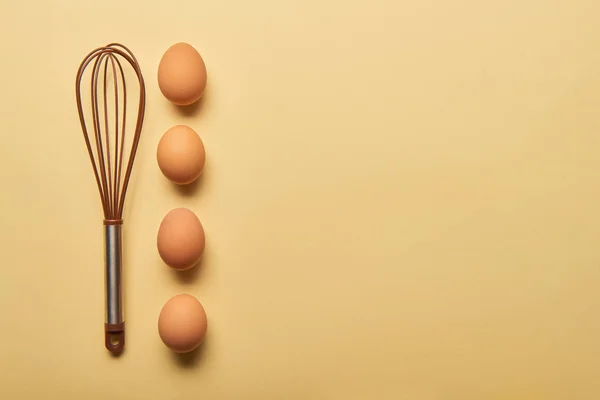 Top view of balloon whisk and eggs  on yellow background — Stock Photo