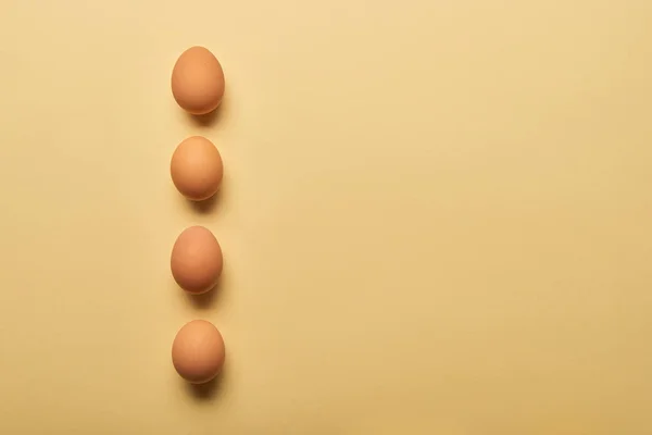 Flat lay with brown organic eggs arranged in vertical row on yellow background — Stock Photo